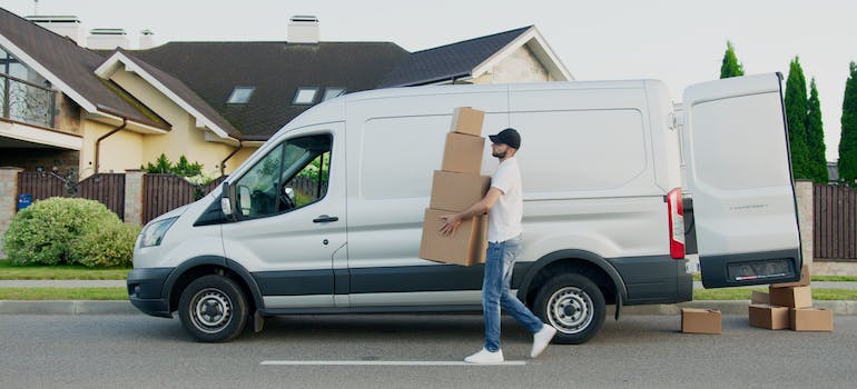 A residential mover carrying boxes in front of a van