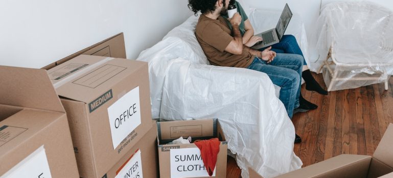 A couple sitting next to boxes in a home packed for moving
