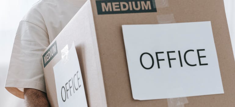 A person carrying a moving box labeled ‘office’