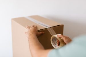 person closing a cardboard box with a duct tape