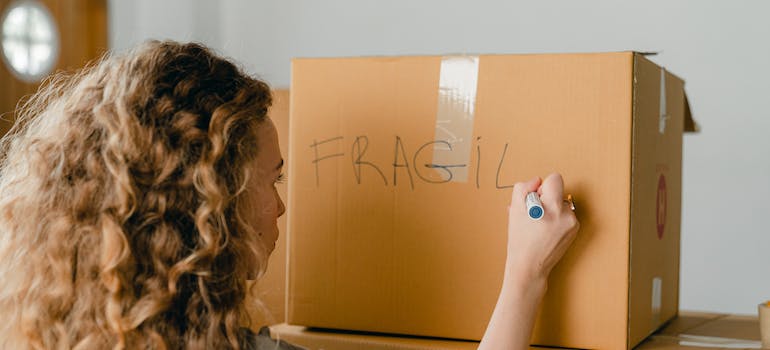 A woman labeling a moving box with the word ‘fragile’