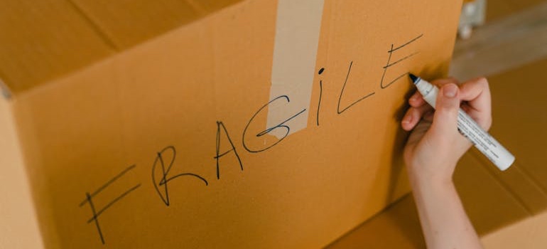 A person writing the word ‘Fragile’ on a box when packing ceramics and porcelain for a move