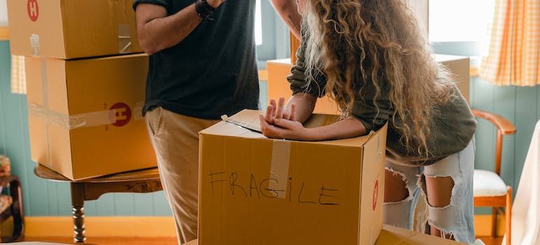 Two people standing next to a moving box labeled "Fragile"