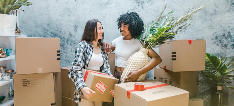 Two women standing next to moving boxes and smiling